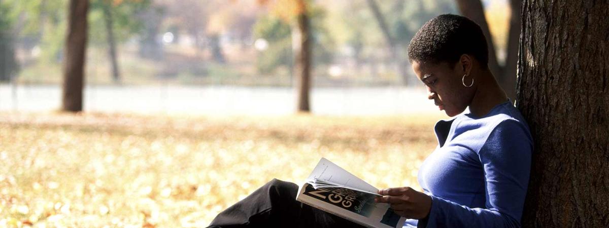 Academic Programs at Minneapolis College student reading a textbook while leaning against a tree.