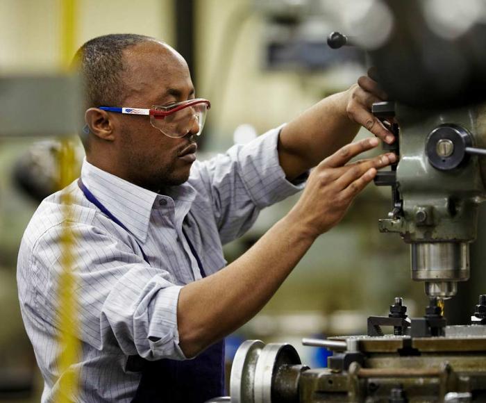 Man working with a drill press in a machine shop at Minneapolis College