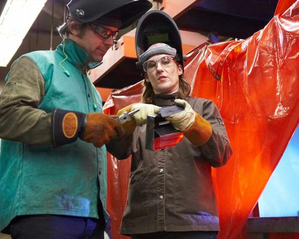 instructor showing student welding solution with student working in the background